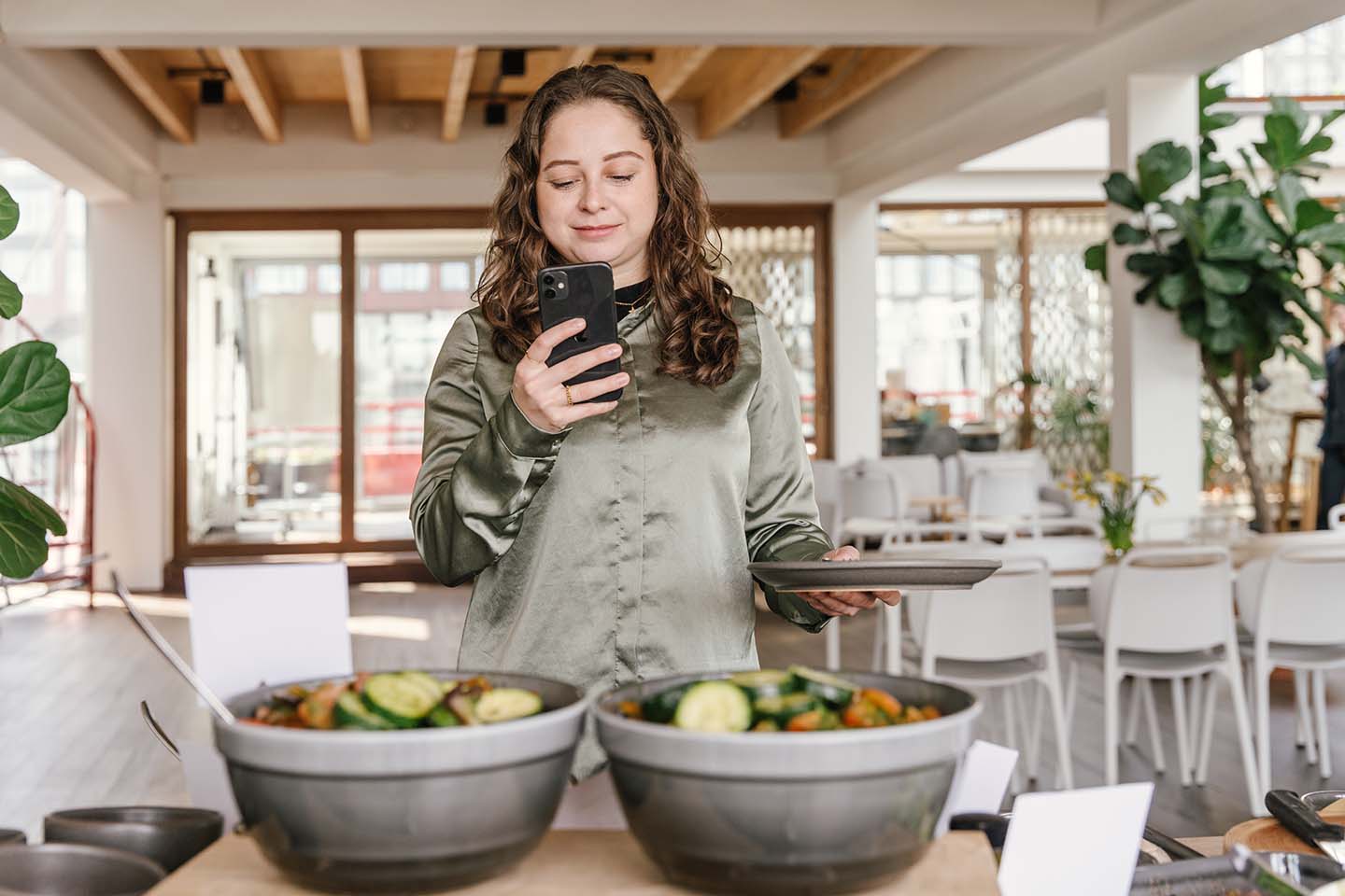 Employee standing in front of buffet in office restaurant looking at the Join Program Food app on her phone